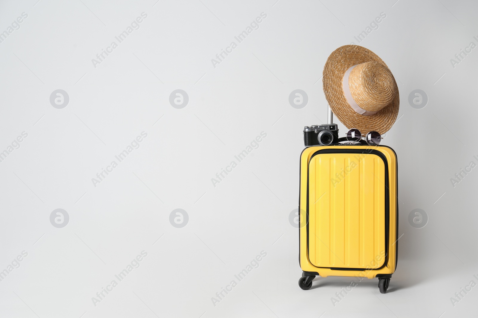 Photo of Travel suitcase with hat, camera and sunglasses on light grey background, space for text. Summer vacation