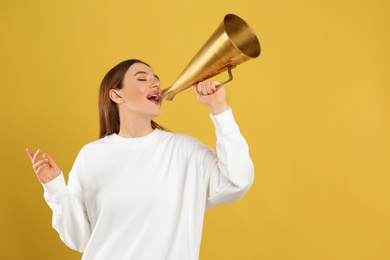 Young woman with vintage megaphone on yellow background