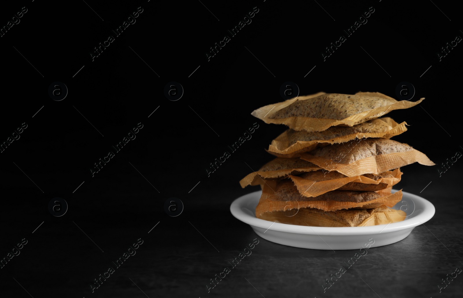 Photo of Saucer with used tea bags on dark table against black background. Space for text