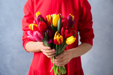 Photo of Woman holding beautiful spring tulips on light blue background, closeup