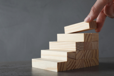 Photo of Woman building steps with wooden blocks on grey table, closeup. Career ladder