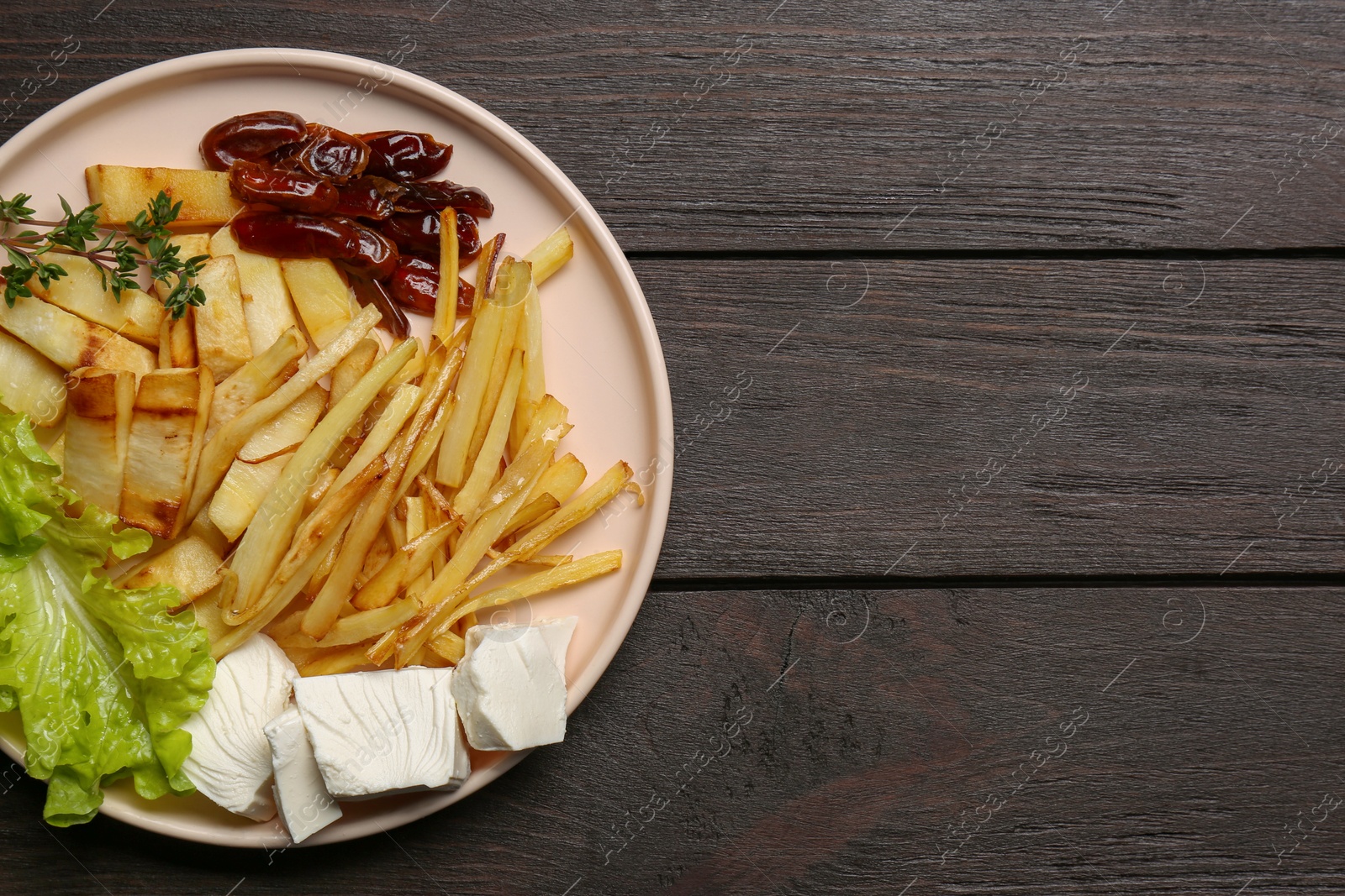 Photo of Delicious parsnip with lettuce, feta cheese and dates on black wooden table, top view. Space for text