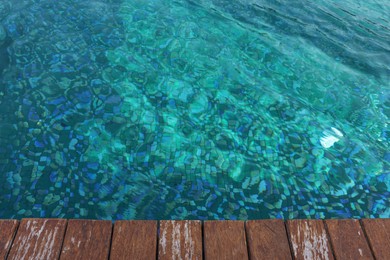 Photo of Clear rippled water in swimming pool and wooden deck outdoors