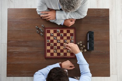Men playing chess during tournament at wooden table, top view