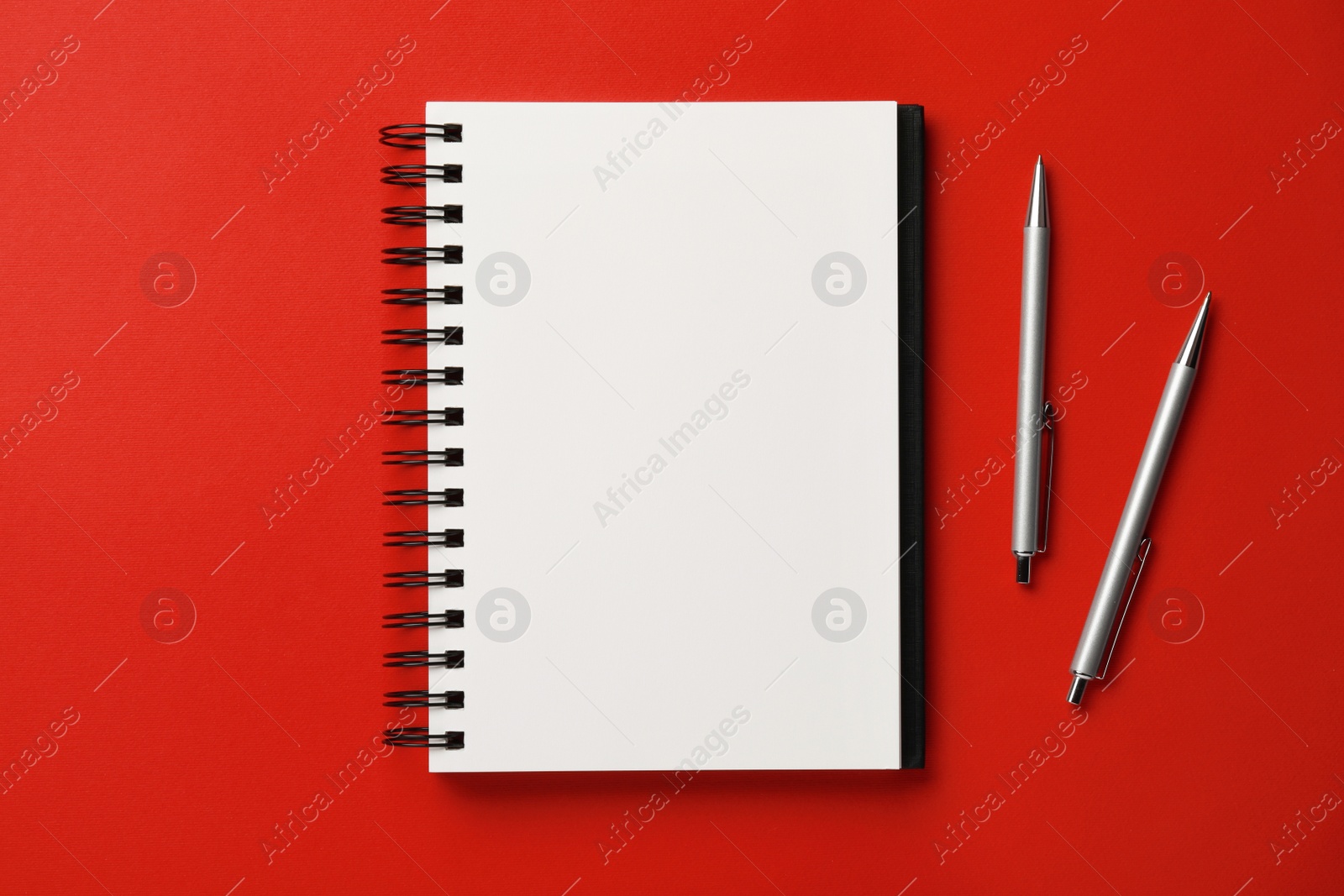 Photo of Notebook and pens on red background, flat lay