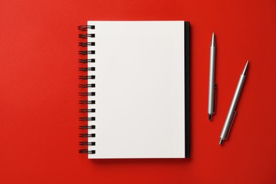 Photo of Notebook and pens on red background, flat lay