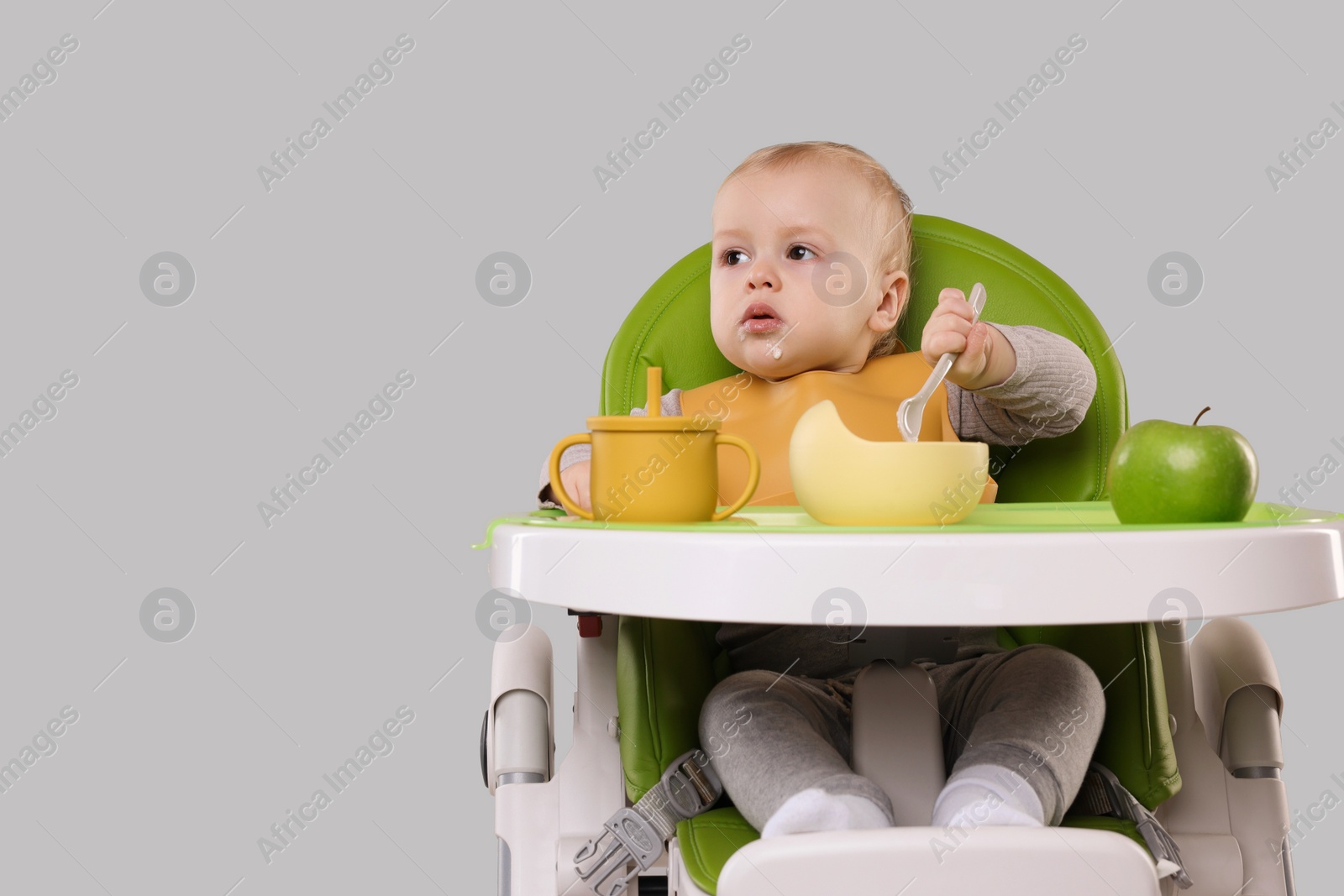 Photo of Cute little baby eating healthy food in high chair on gray background, space for text