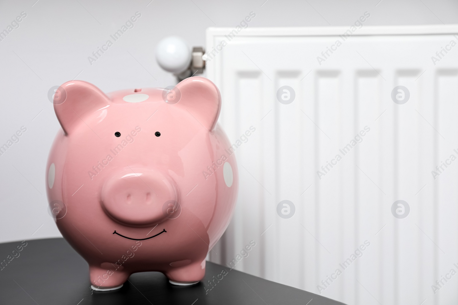 Photo of Piggy bank on black table near heating radiator, space for text