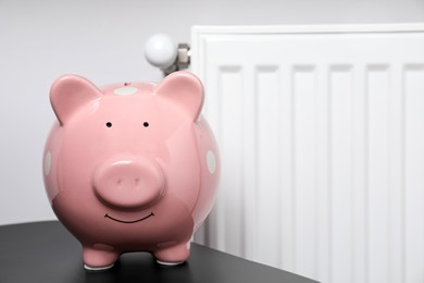 Photo of Piggy bank on black table near heating radiator, space for text