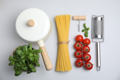 Photo of Composition with uncooked spaghetti and cooking utensils on white background, top view