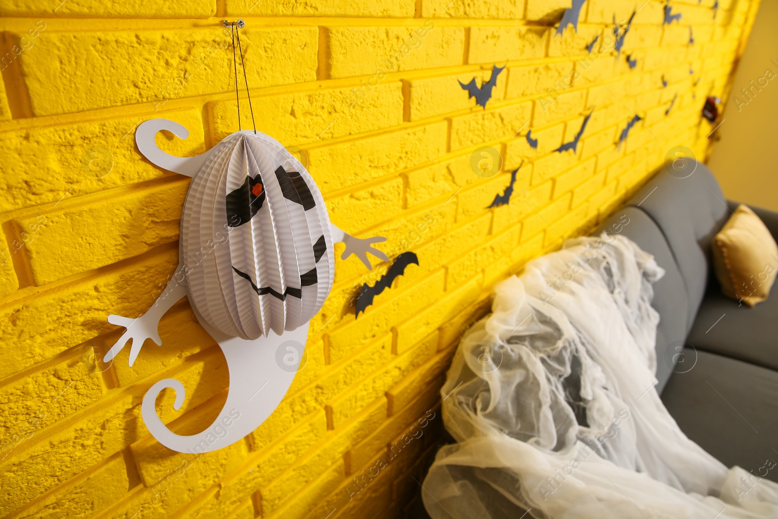 Photo of Yellow brick wall decorated for Halloween in room, focus on cute ghost