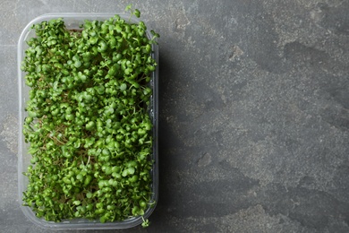 Photo of Sprouted arugula seeds in plastic container on grey table, top view. Space for text