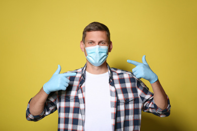 Photo of Male volunteer in mask and gloves on yellow background. Protective measures during coronavirus quarantine