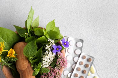 Photo of Wooden mortar with fresh herbs, flowers and pills on white table, top view. Space for text