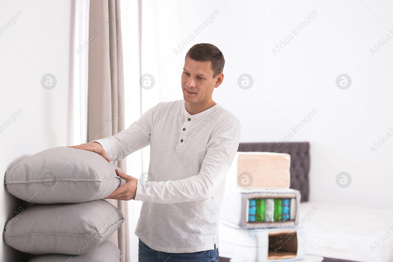 Photo of Happy man choosing cushion in mattress store