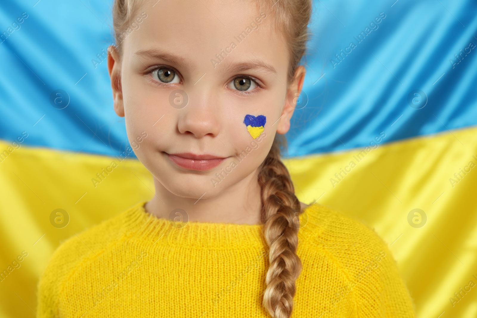 Photo of Little girl with face paint near Ukrainian flag, closeup