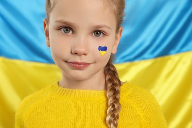 Little girl with face paint near Ukrainian flag, closeup