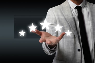 Image of Quality rating. Man showing stars on virtual screen against dark background, closeup