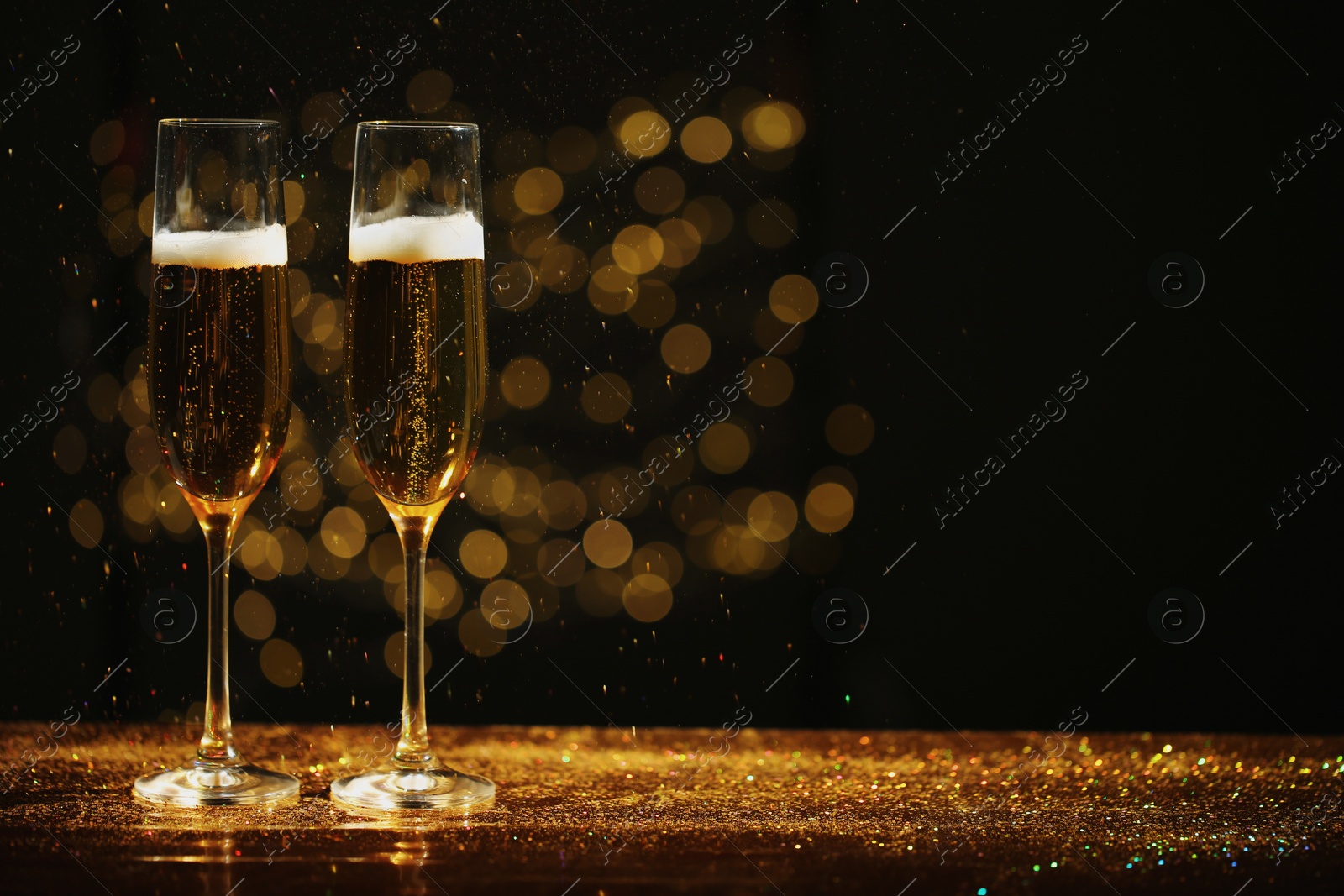 Photo of Glasses of champagne and golden glitter on table against blurred background. Space for text