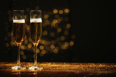 Glasses of champagne and golden glitter on table against blurred background. Space for text