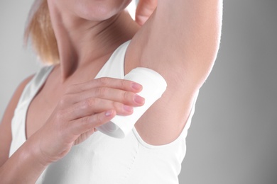 Young woman using deodorant on grey background, closeup