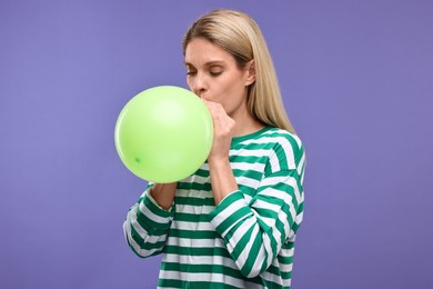 Photo of Woman blowing up balloon on violet background