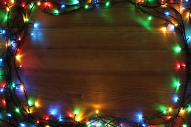 Photo of Frame of colorful Christmas lights on wooden table, top view. Space for text