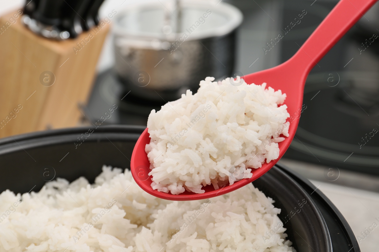 Photo of Spoon with boiled rice over cooker against blurred background, closeup