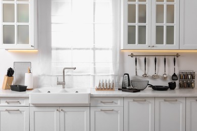 Photo of Set of different utensils near sink on countertop in kitchen