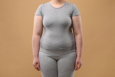 Overweight woman in grey clothes on beige background, closeup