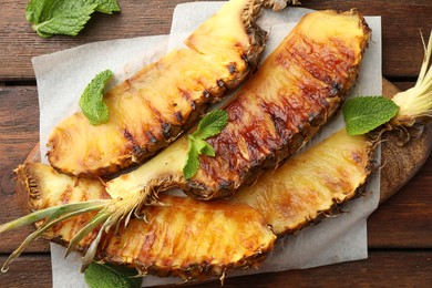 Tasty grilled pineapple pieces and mint leaves on wooden table, flat lay