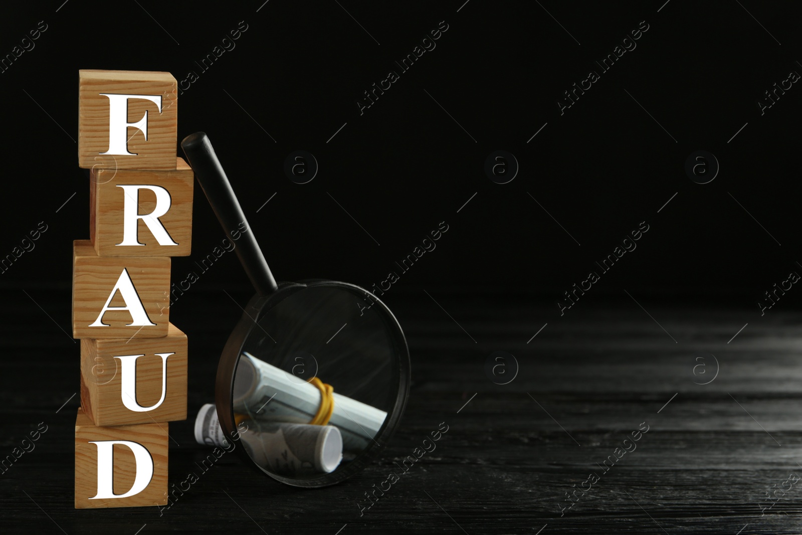 Photo of Wooden cubes with word Fraud, magnifying glass and money on black table, space for text