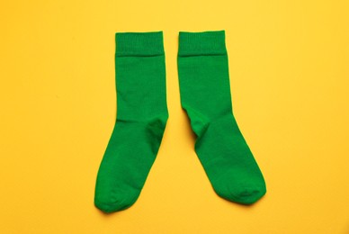 Photo of Green socks on yellow background, flat lay