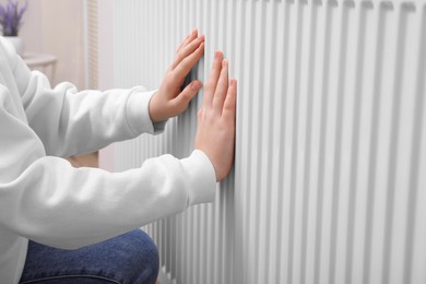 Girl warming hands on heating radiator indoors, closeup