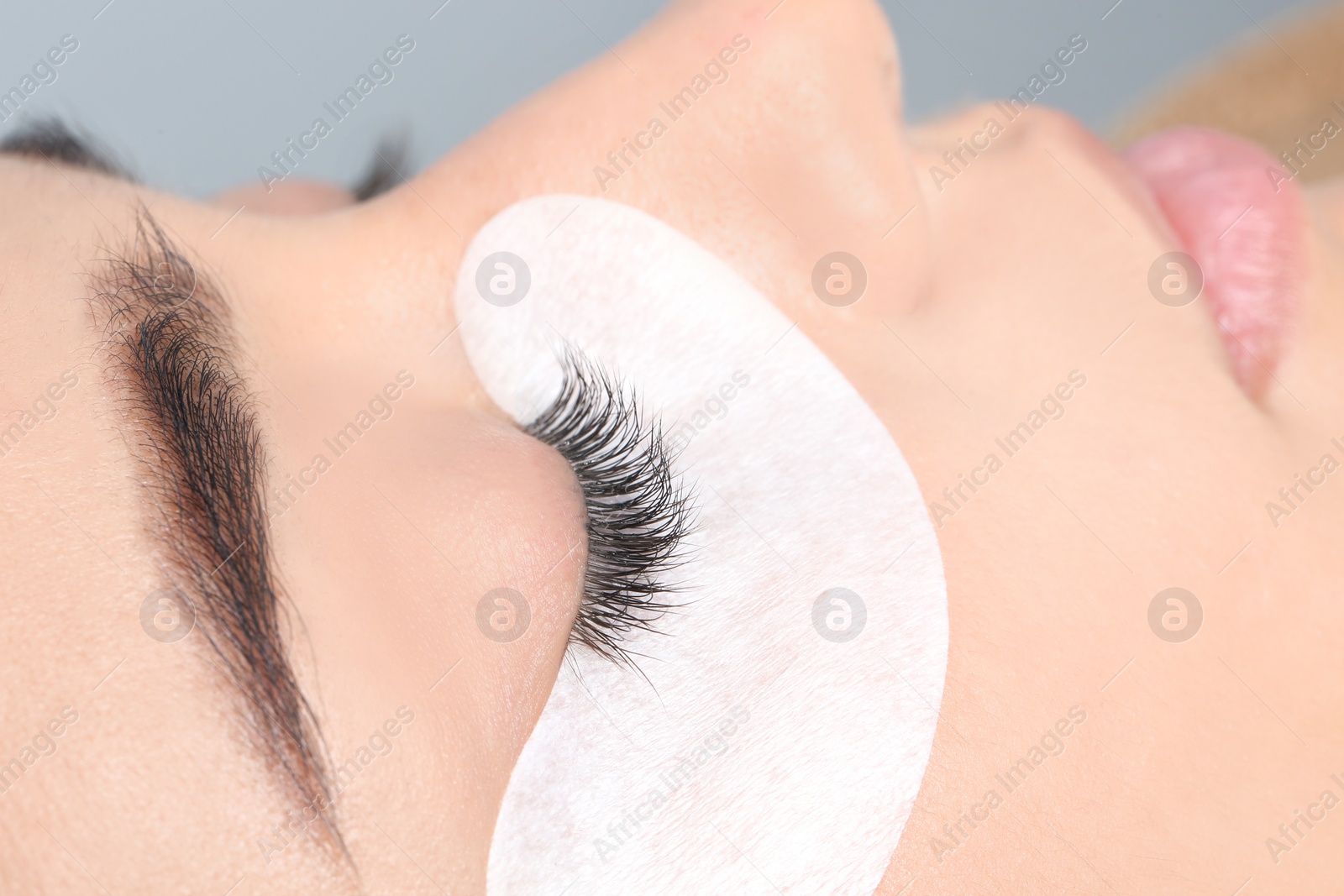 Photo of Young woman undergoing eyelashes extensions procedure, closeup