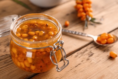 Delicious sea buckthorn jam and fresh berries on wooden table, closeup. Space for text