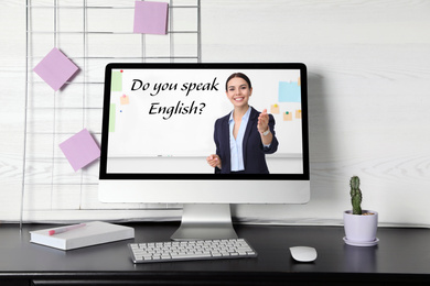 Image of Modern computer for online English learning with teacher on table indoors