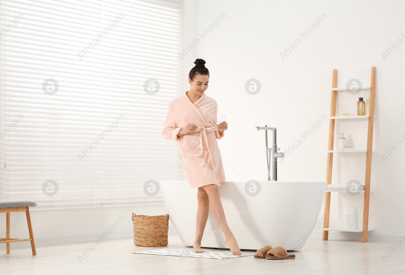 Photo of Beautiful happy woman wearing stylish bathrobe near tub in bathroom