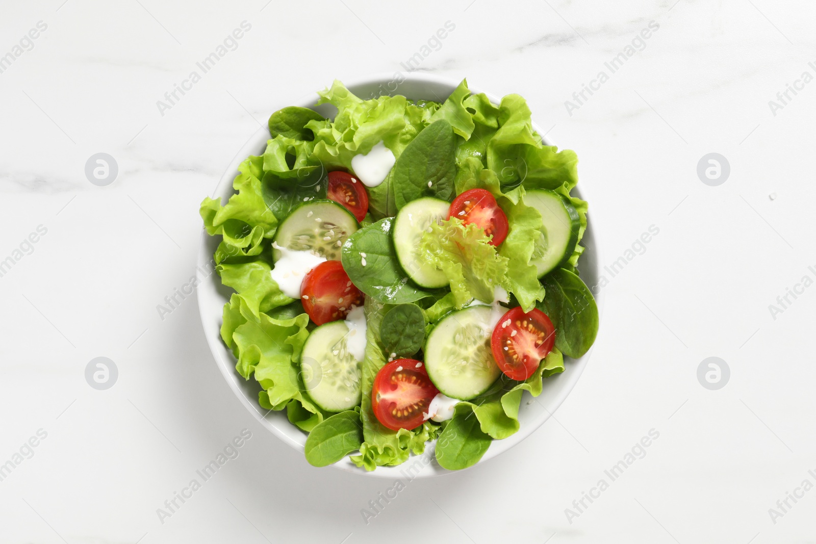 Photo of Delicious salad in bowl on white marble table, top view