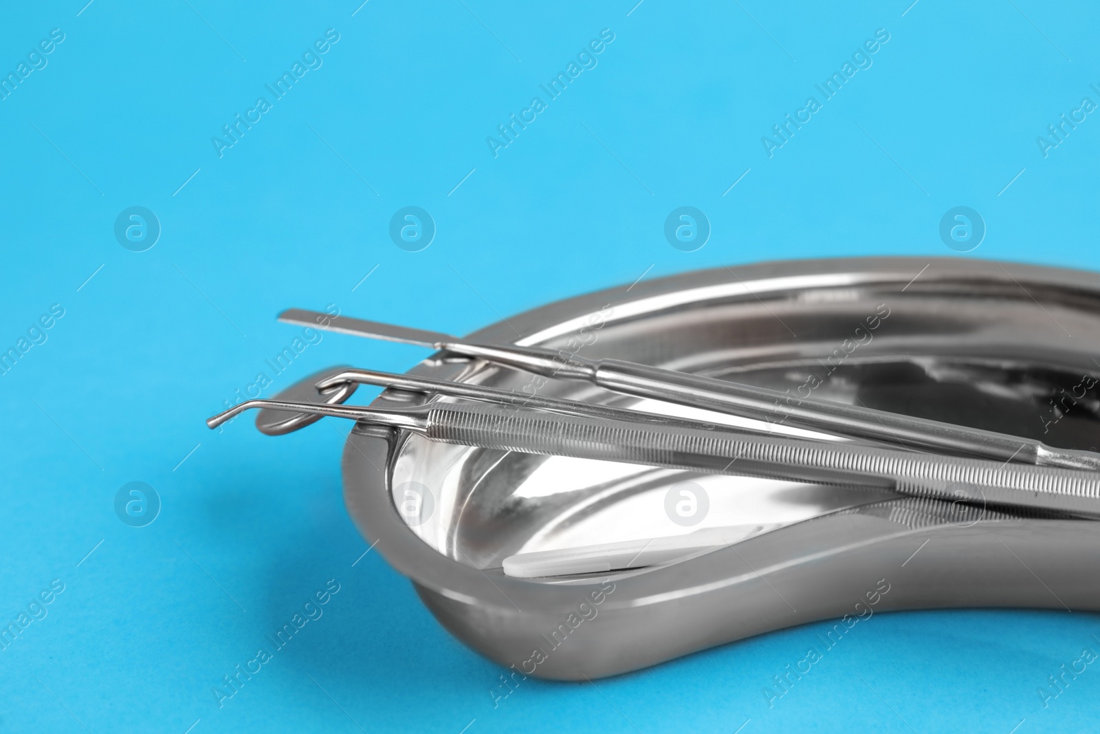 Photo of Kidney shaped tray with set of dentist's tools on light blue background, closeup