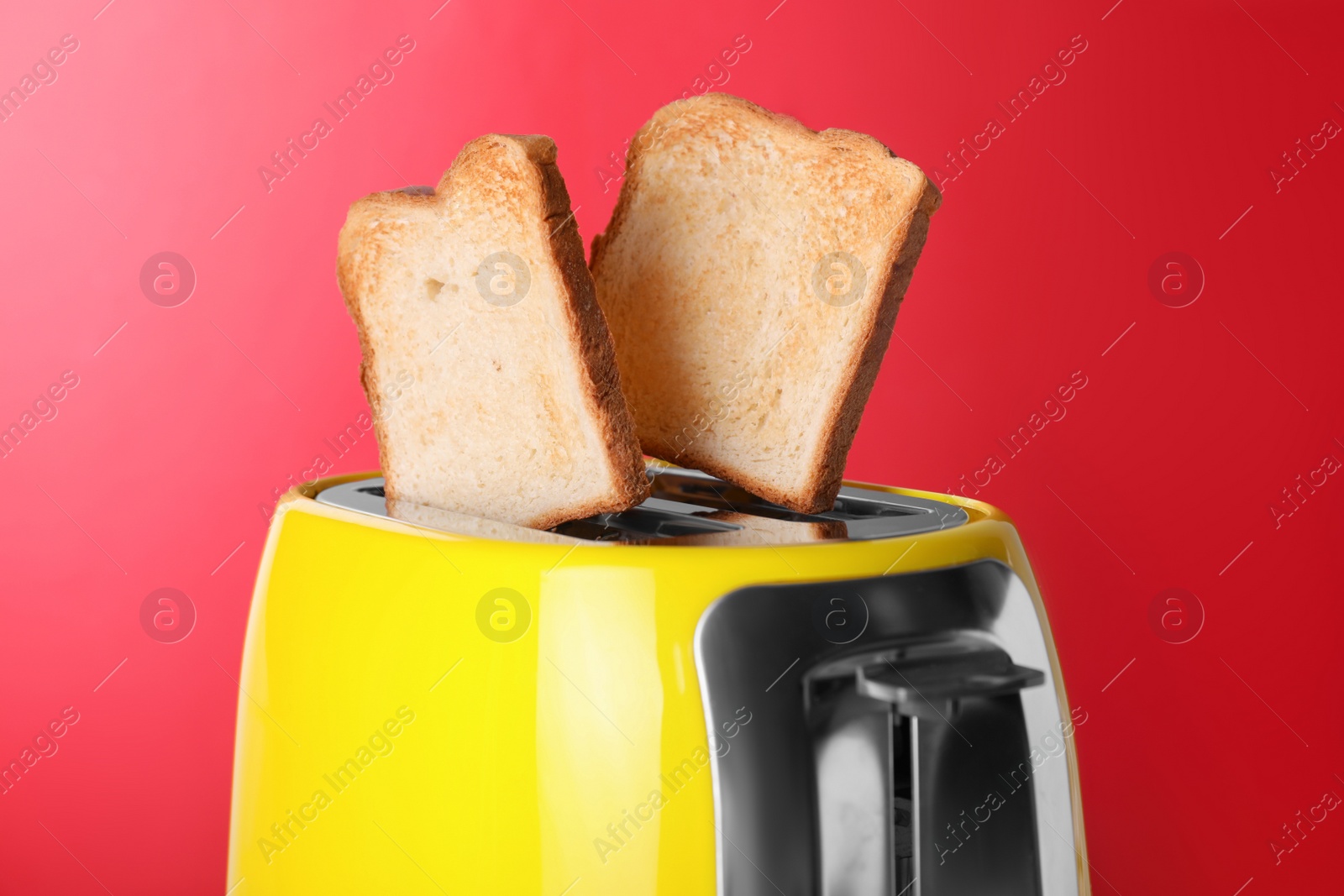 Photo of Yellow toaster with roasted bread against red background, closeup