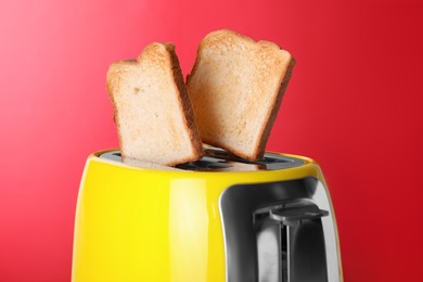 Photo of Yellow toaster with roasted bread against red background, closeup