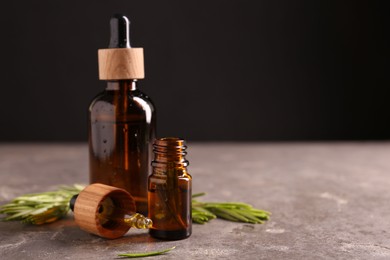 Essential oil in bottles, dropper and rosemary on grey table, space for text