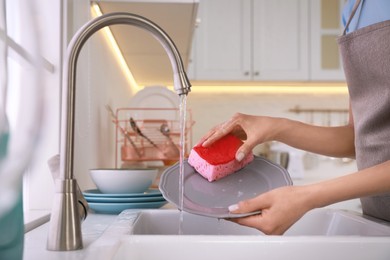 Woman washing plate above sink in kitchen, closeup