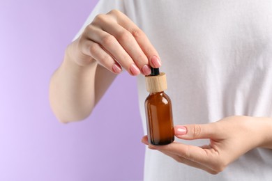 Photo of Woman holding bottle with serum against lilac background, closeup