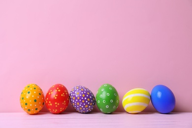 Photo of Decorated Easter eggs on table near color wall. Space for text