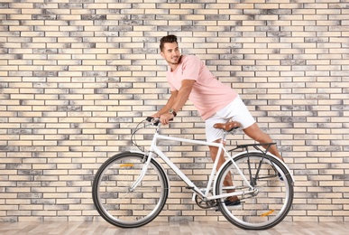 Photo of Handsome young hipster man riding bicycle near brick wall