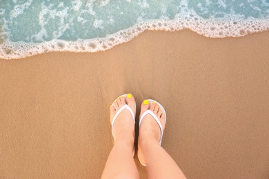 Photo of Top view of woman with white flip flops on sand near sea, space for text. Beach accessories