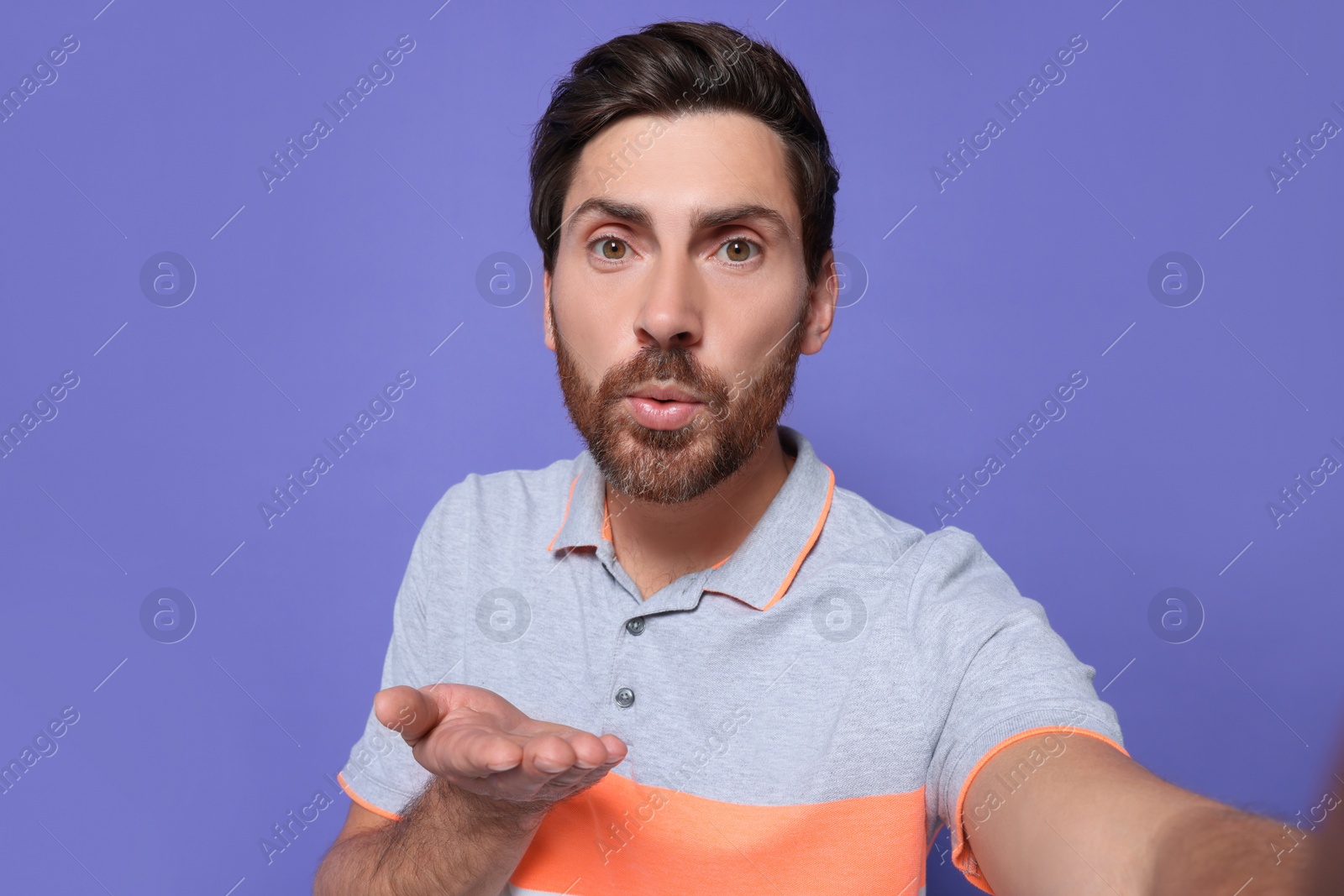 Photo of Handsome man blowing kiss while taking selfie on violet background. Space for text