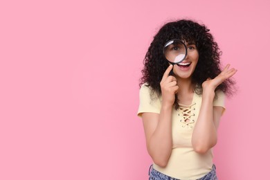 Photo of Happy young woman looking through magnifier glass on pink background. Space for text
